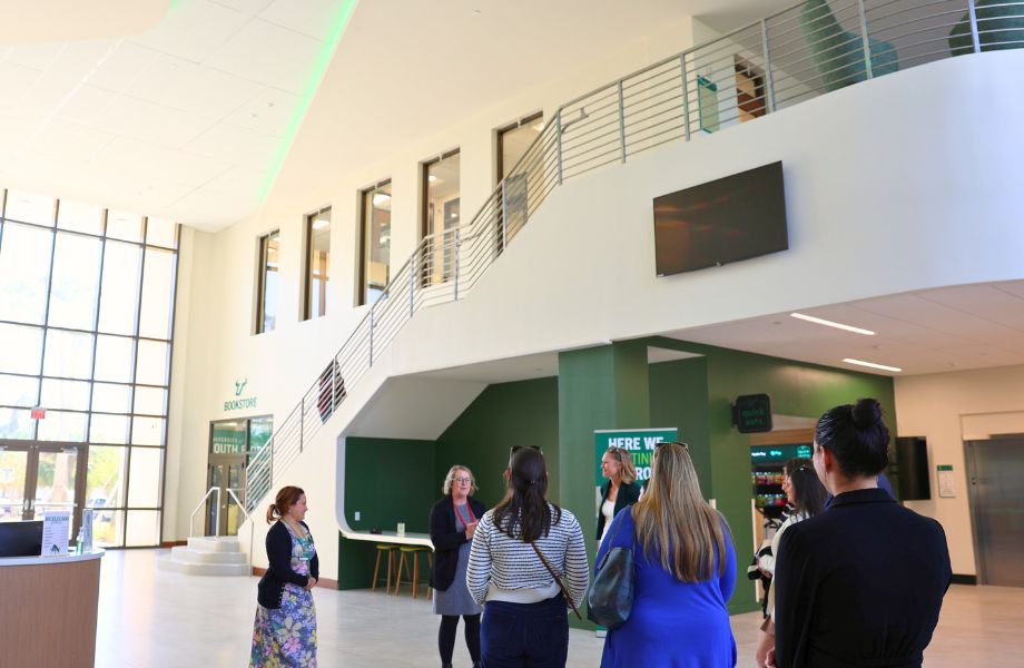 Honors faculty and staff receiving a tour of Atala Hall from Dr. Cayla Lanier. Bright light coming in from tall windows and a feature stair case.
