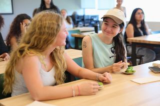 Two students share a smile as they eat samples from a sustainable tasting plate.