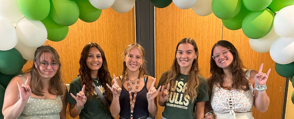Incoming students smile under a green and white balloon arch.