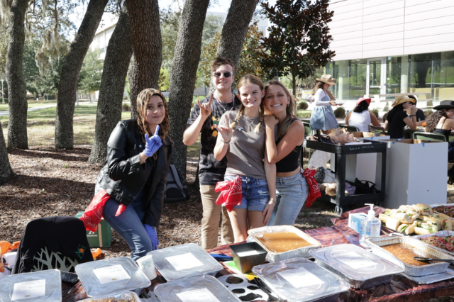 Student council members smile for a photo in front of trays of food at the honors fall rodeo