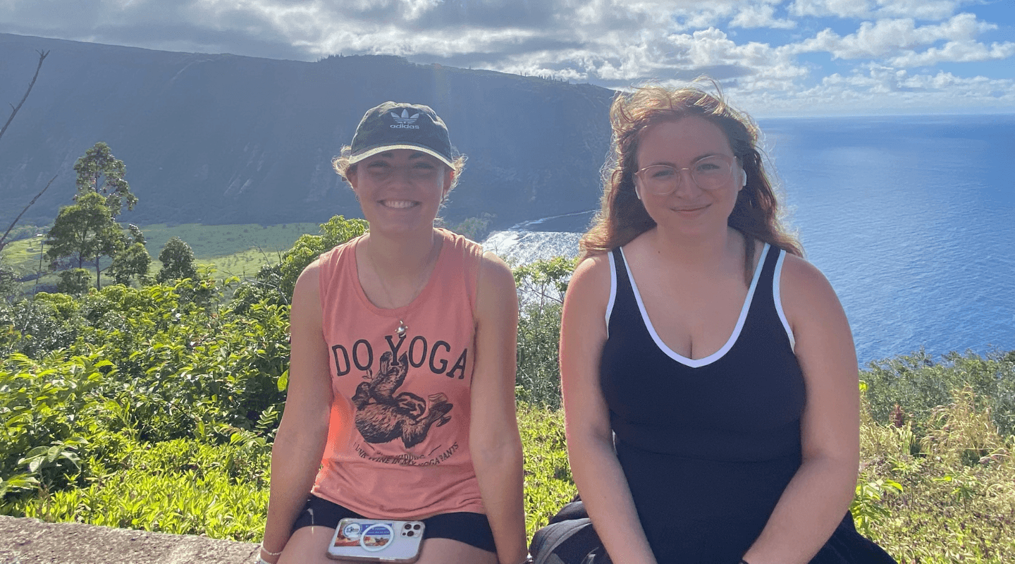 Two Honors students smile in front of mountainous Hawaiian landscape