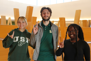Nora Wolfgang, Marco Nardiello, and Whitney Louis pose while making Go Bulls signs in the Judy Genshaft Honors College.