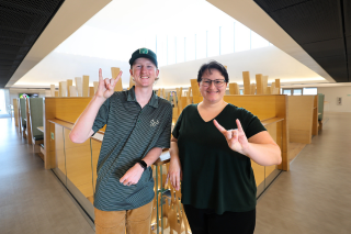 Adam Costello and Kate Ashmore smile with the "Go Bulls" hand sign in the Honors building.