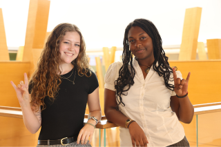 Kelsey Sherman and Elise Prophete pose in the Honors building with the "go bulls" sign.