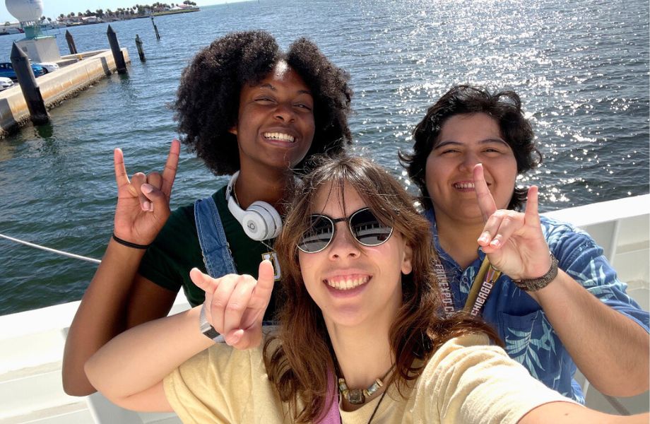 Josephine Combs and other Honors students posing with the "Go Bulls" hand sign by the ocean.