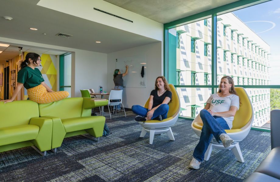 Honors students hanging out in Osprey Hall with lounge seating and a view of the water from the window