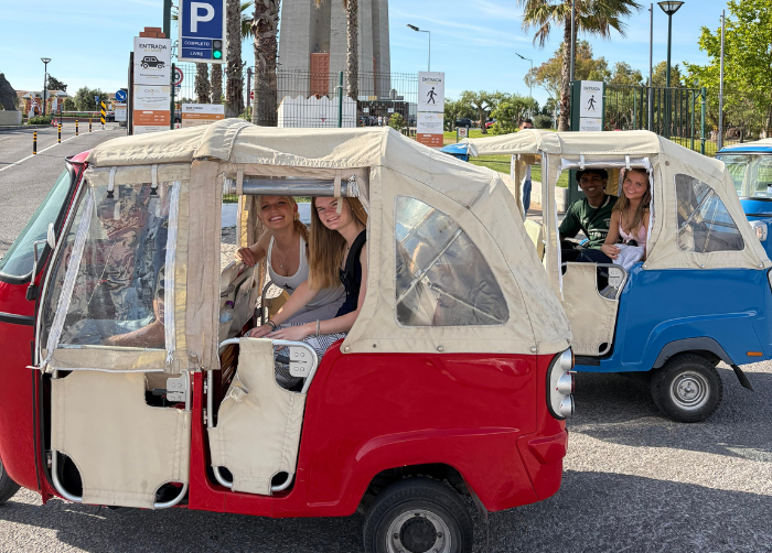 Two pairs of students sitting in their respective cars posing for a photo.