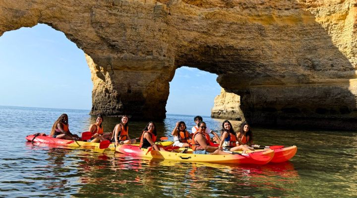 Honors students kayaking under a rocky cliff in blue waters.