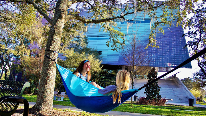 Two honors students sit in a hammock outside the new Honors College building.