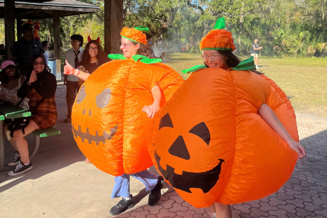 Two students in inflatable pumpkin costumes run hand in hand at the 2023 Pumpkin Palooza