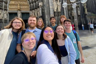 A group of Judy Genshaft Honors College students take a selfie photograph while smiling outside of a church