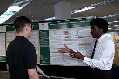 Student presenting in front of a research poster to an attendee at Summer Undergraduate Research Symposium