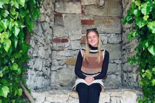 Taylor Herman sitting in a stone alcove, surrounded by green ivy.