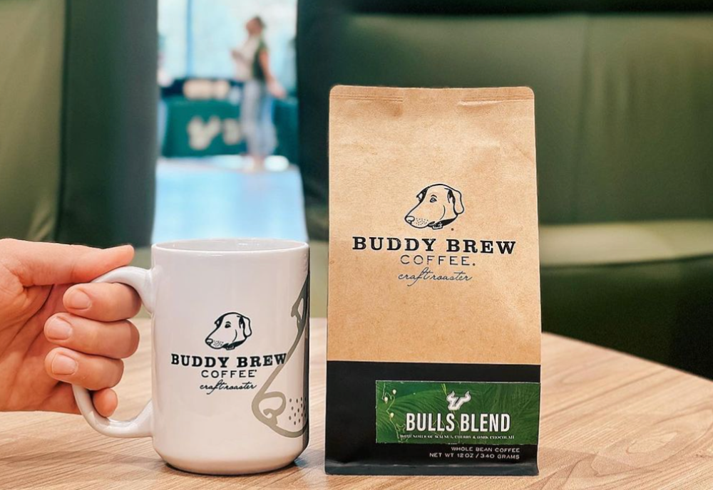 A person holds a buddy brew coffee mug next to a bag of the new buddy brew bulls blend. 