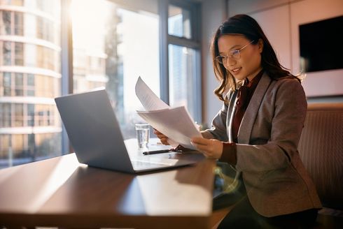 Smiling businesswoman seated in front of laptop and holding papers.