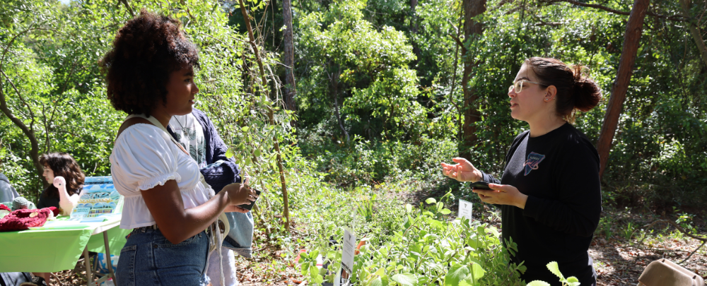 Two students converse in front of a wooded area at the 2024 USF Climate Teach-In Farmers Market