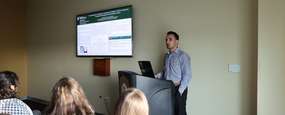 A male student presents his climate research to a group of seated students at the 2024 USF Climate Teach-In Research Fair.
