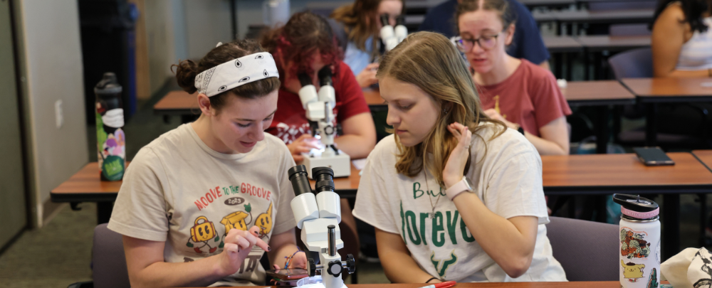 Two students work seated a microscope during a microplastics lab hosted by Tampa Bay Watch at the 2024 USF Climate Teach-In