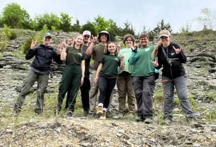 A group of seven Judy Genshaft Honors students and Dr. Lydia Wassink make the Go Bulls sign while standing near a fossil site as part of the Fossil Hunters study away trip.
