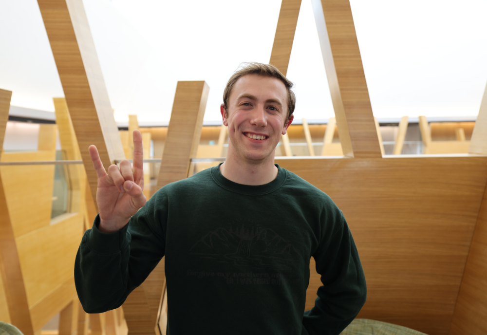 Judy Genshaft Honors College student Kobe Phillips poses in the Honors building while making a Go Bulls sign.