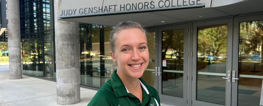 Hannah Craig smiles in front of the Judy Genshaft Honors College