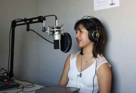 Sophia Montejo wears headphones while sitting in front of a microphone. 
