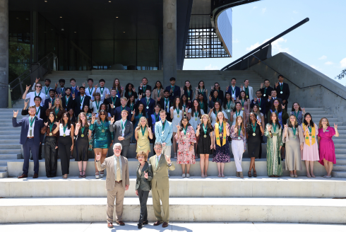 A large group photo of Spring 2024 USF Judy Genshaft Honors College students as 70 graduate pose on a tiered staircase while making a Go Bulls sign.