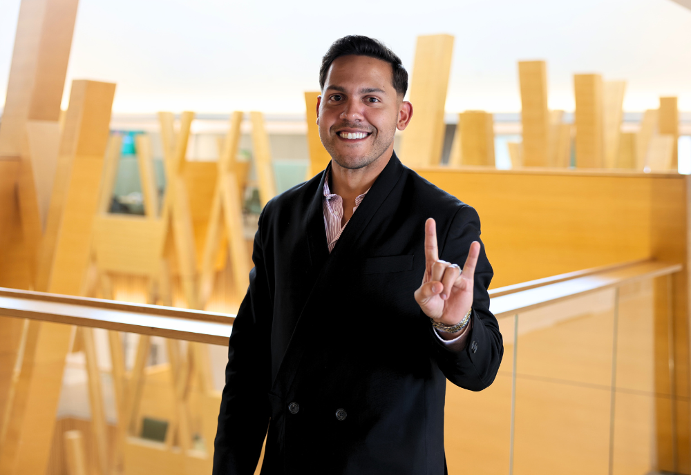 USF alum Hiram Rios Hernandez poses while making a Go Bulls sign in the Judy Genshaft Honors College building.