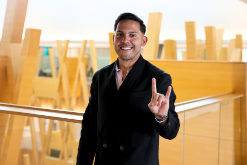 USF alum Hiram Rios Hernandez poses while making a Go Bulls sign in the Judy Genshaft Honors College building.