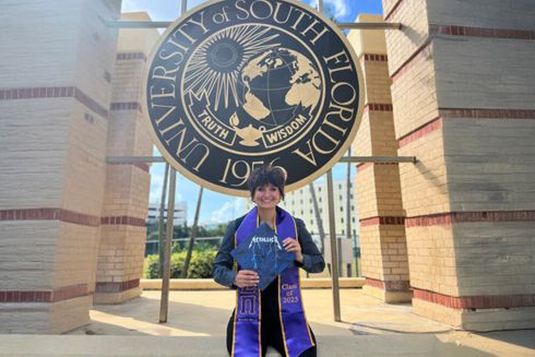 Brooke Elrod poses with her graduation cap - with Metallica decoration - in front of a USF sign.
