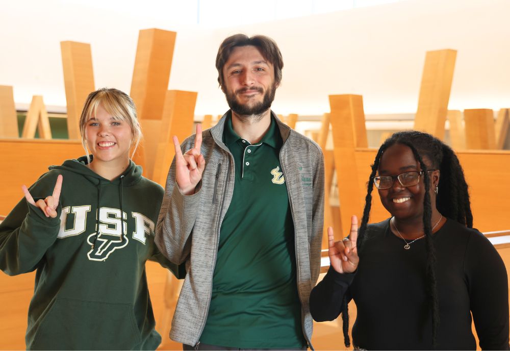 Nora Wolfgang, Marco Nardiello, and Whitney Louis pose for a photo on the fifth floor of the Honors building, holding up the "go bulls" hand sign.