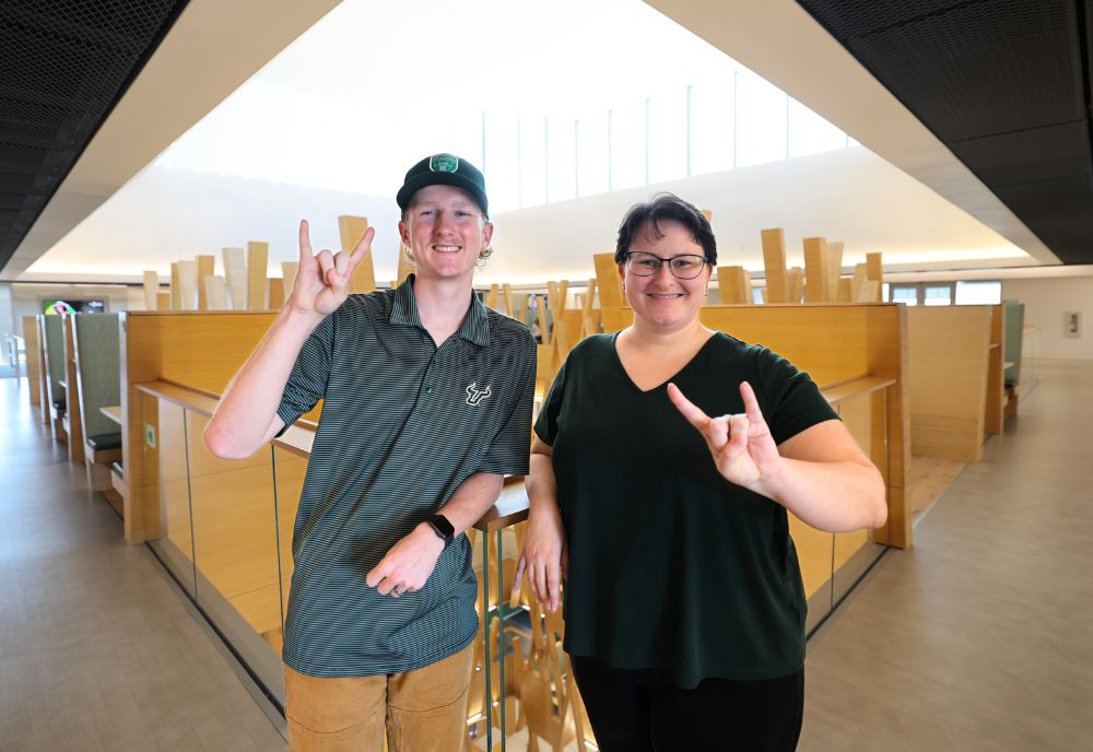 Adam Costello and Kate Ashmore smile with the "Go Bulls" hand sign in the Honors building.