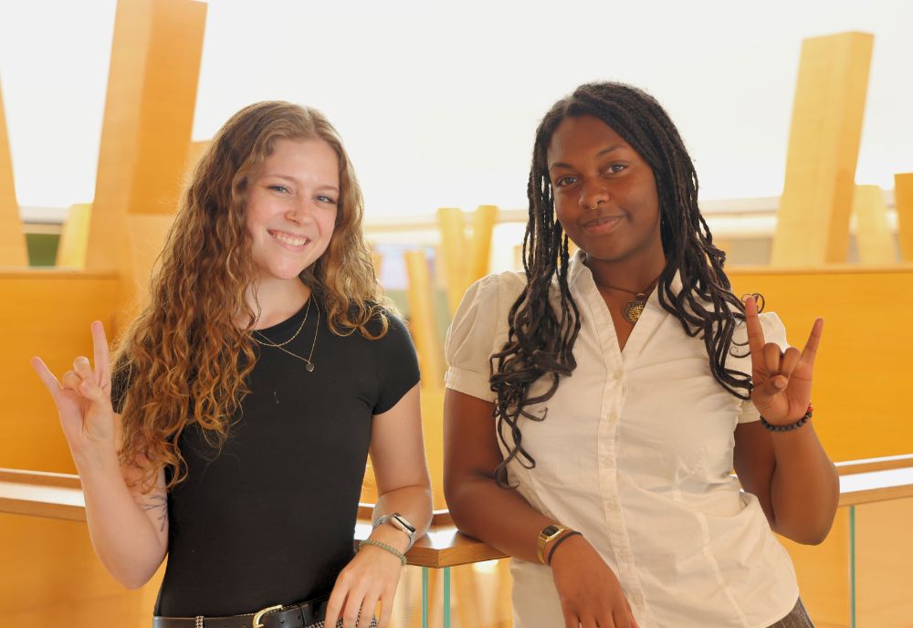 Kelsey Sherman and Elise Prophete pose in the Honors building with the "go bulls" sign.