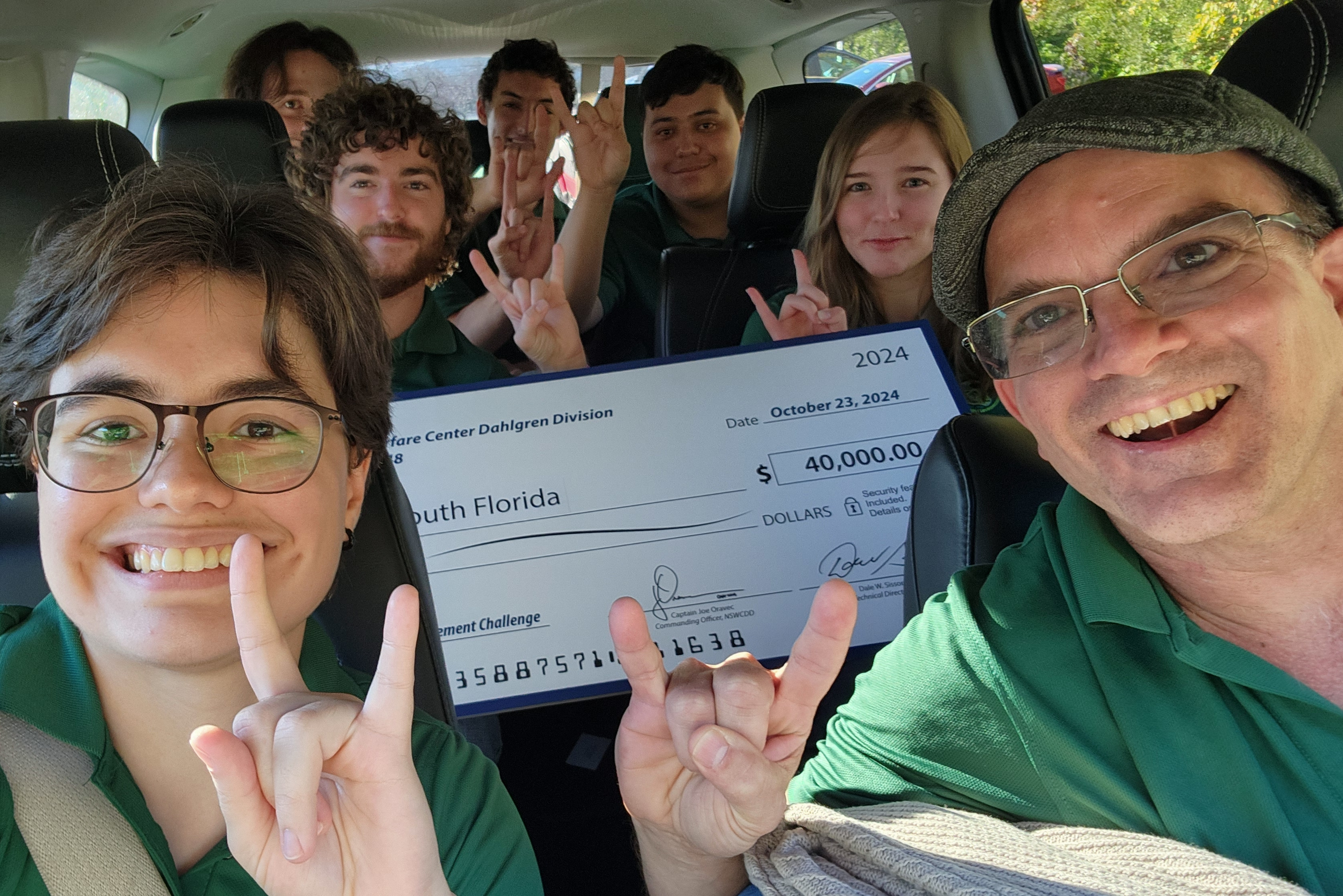 Michelle McAveety and other cybersecurity students and a faculty member pose with a 40,000 dollar check in a vehicle.