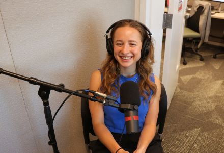 Mira Stimac smiling in the Honors AV room, wearing a headset for the podcast.