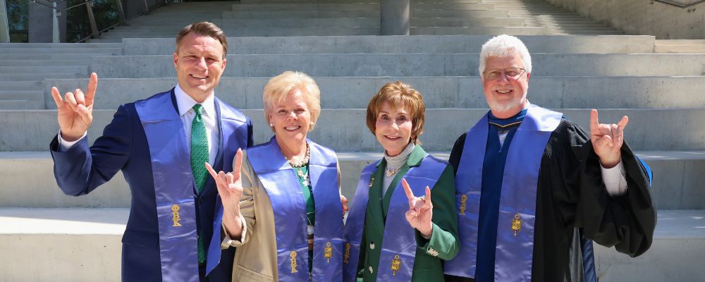 USF Board of Trustees Chair Will Weatherford, President Rhea Law, President Emerita Judy Genshaft, and Honors Dean Charles Adams pose with the "go bulls" sign outside the Honors amphitheater.
