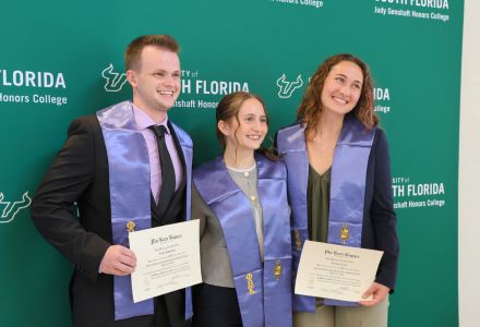 Three Phi Beta Kappa inductees pose for a photo in front of the USF backdrop