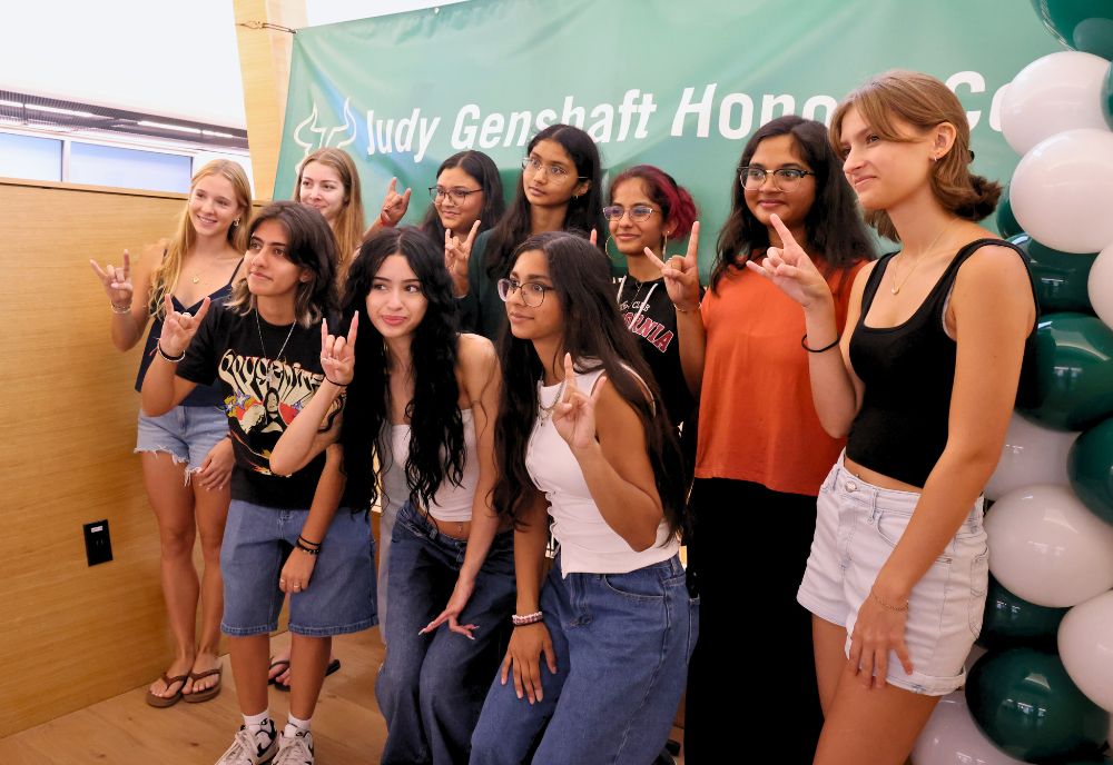 Honors students pose in a fifth floor learning loft with the "Go Bulls" hand sign in front of a Judy Genshaft Honors College green banner and a green and white balloon tower.