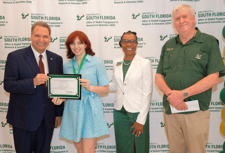 Chloe Jones holds OneUSF Undergraduate Research Excellence Award accompanied by USF President Moez Limayem, Dr. Saundra Johnson-Austin, and another university official.