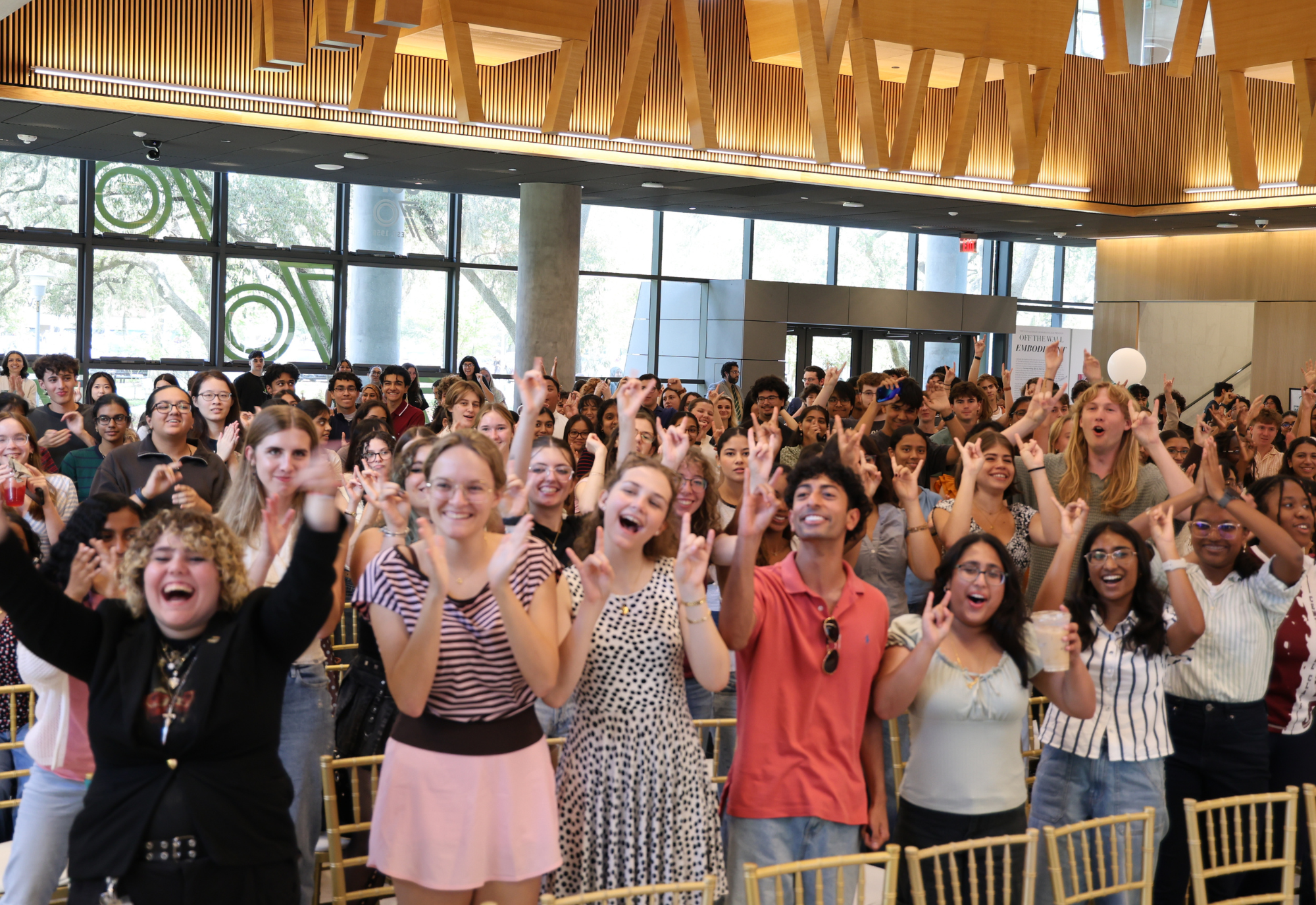 Students cheering with the Go Bulls hand sign in the Judy Genshaft Honors College Zimmerman Family Atrium
