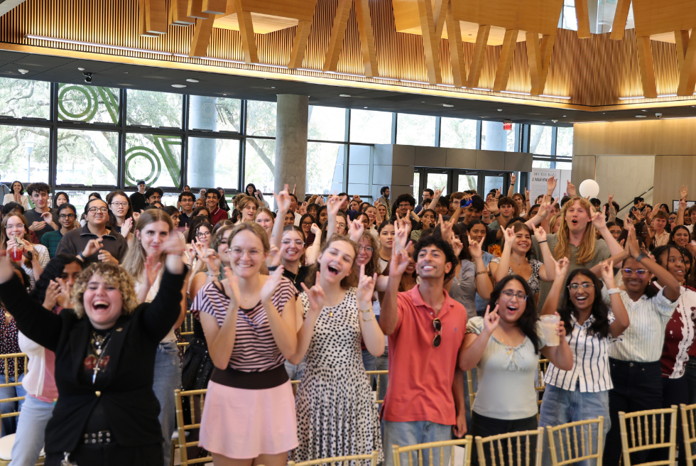 Students cheering with the Go Bulls hand sign in the Judy Genshaft Honors College Zimmerman Family Atrium