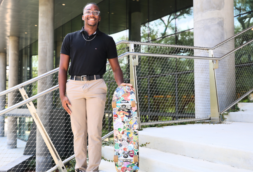DJ Bernadotte poses with his sticker-covered skateboard on the steps of the Judy Genshaft Honors College