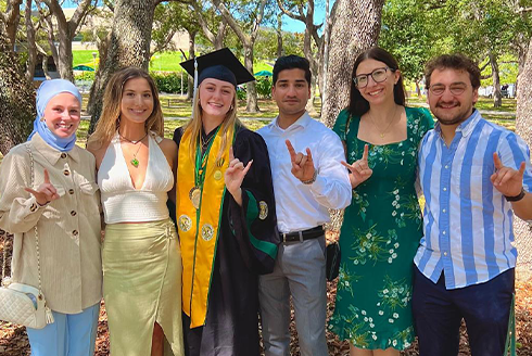 Taylor Herman in a graduation stole and gown with a group of people smiling and holding up