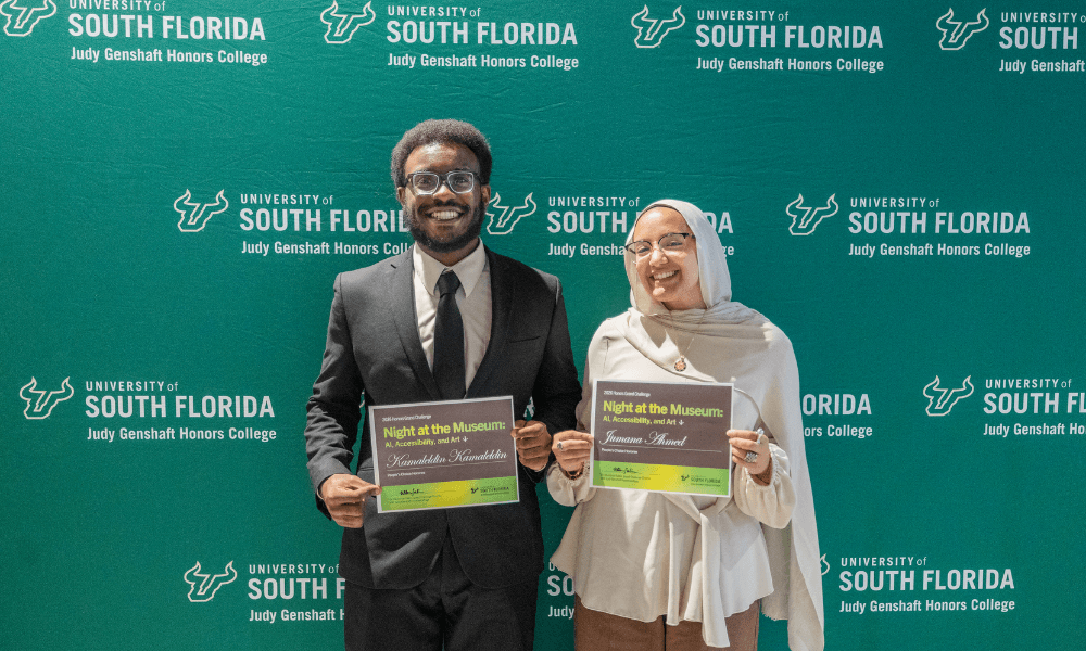 Kamaledin Kamaledin and Jumana Ahmed pose in front of a green USF Honors backdrop holding Grand Challenge certificate