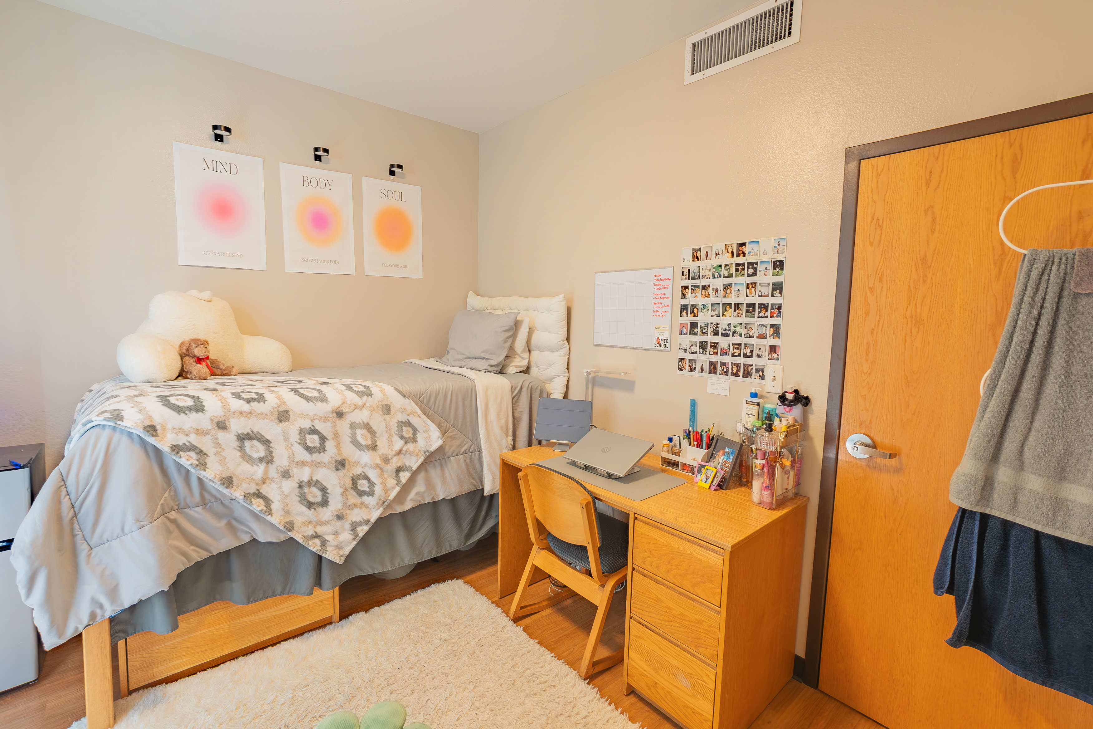 Bedroom with a bed, desk, dresser. Poster of a sunset above the bed.