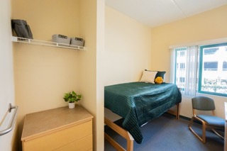 Closet and dresser on left side with tall bed and desk chair.