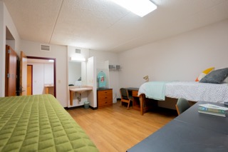 Two beds and desks in foreground, a sink and door to a bathroom in the background.