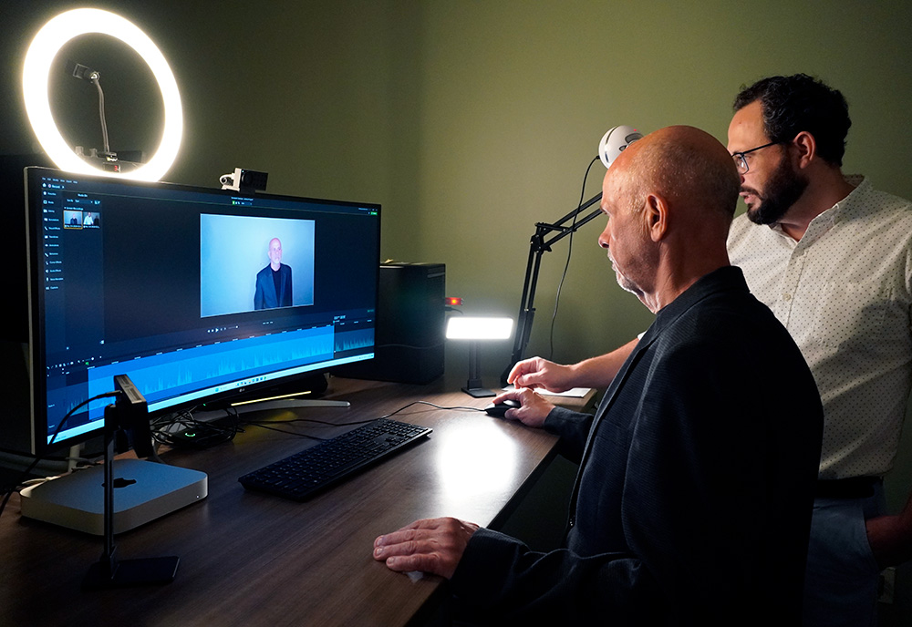 faculty member stands in front of computer screen and is being taught how to use the camera by digital learning training and support member
