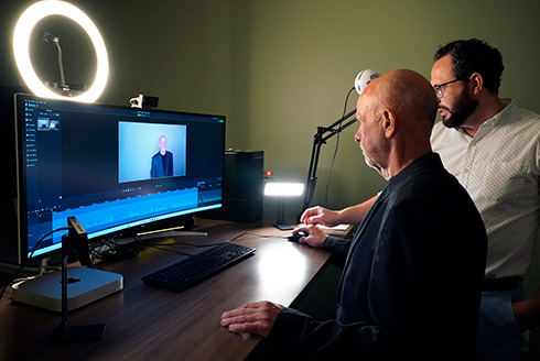 faculty member stands in front of computer screen and is being taught how to use the camera by digital learning training and support member