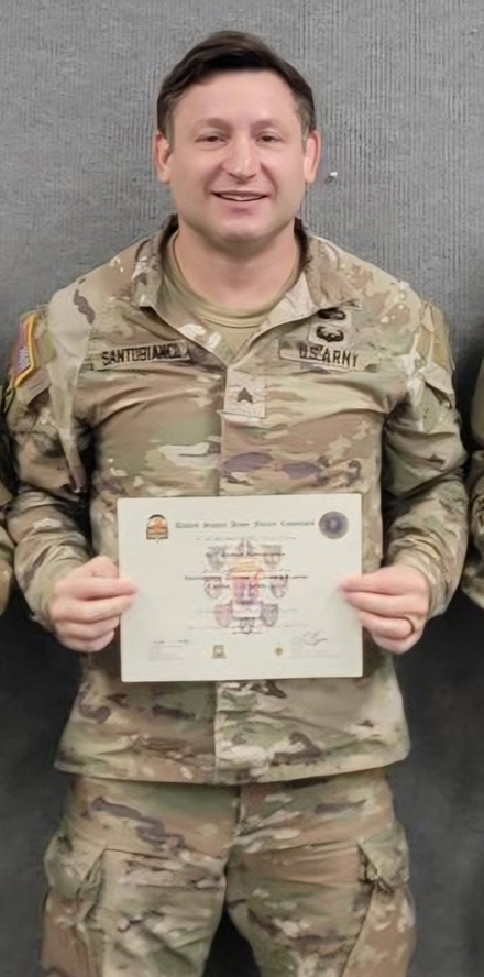Josh Santobianco stands in his military fatigues holding a certificate